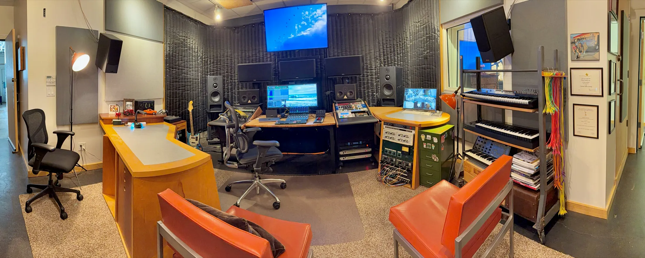 Mix stage with orange client chairs, PMC monitors, AVID control surfaces, and picture wall